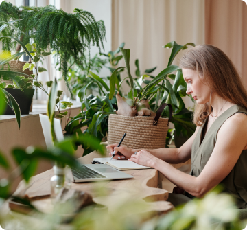 A woman writing on a notebook surrounded by plants